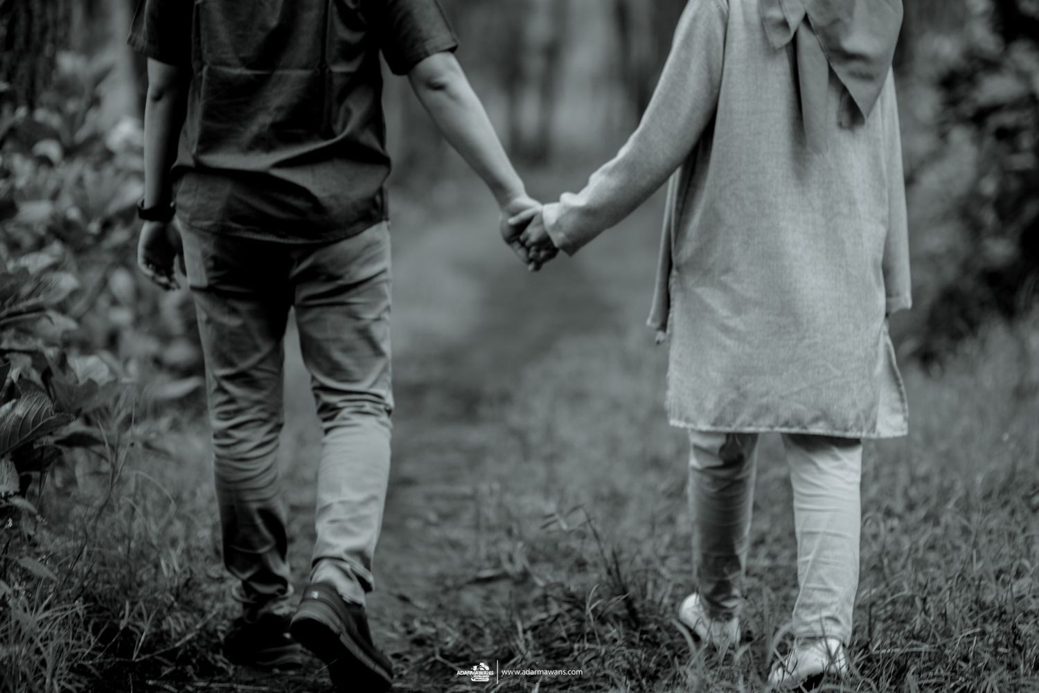 A black and white image of two people holding hands while walking in nature.