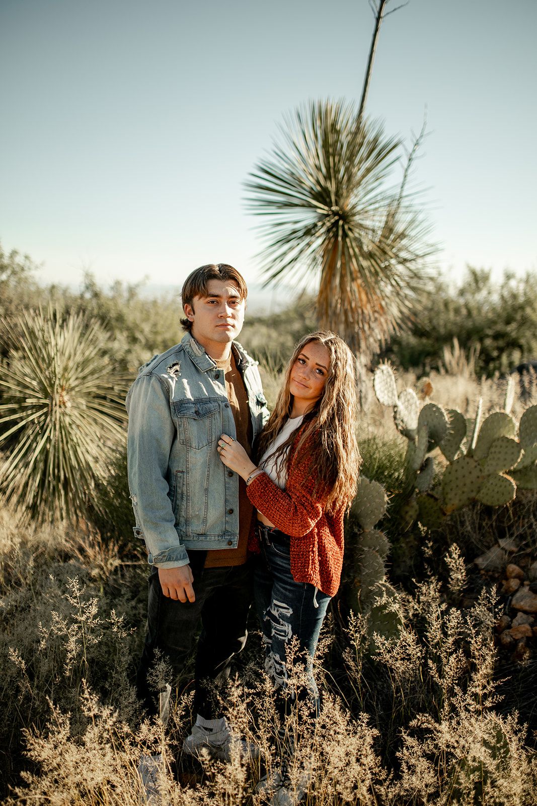 A couple poses among desert plants and cacti during golden hour.