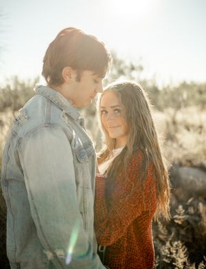 A romantic couple stands close together in the golden desert sunlight with desert plants in the background.