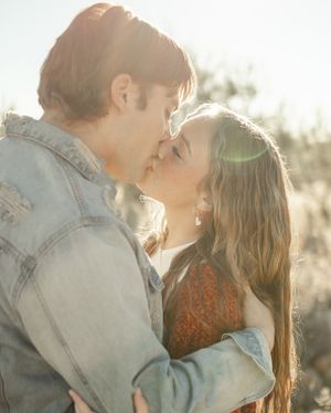 A tender romantic moment between a couple backlit by warm sunlight in a desert setting.