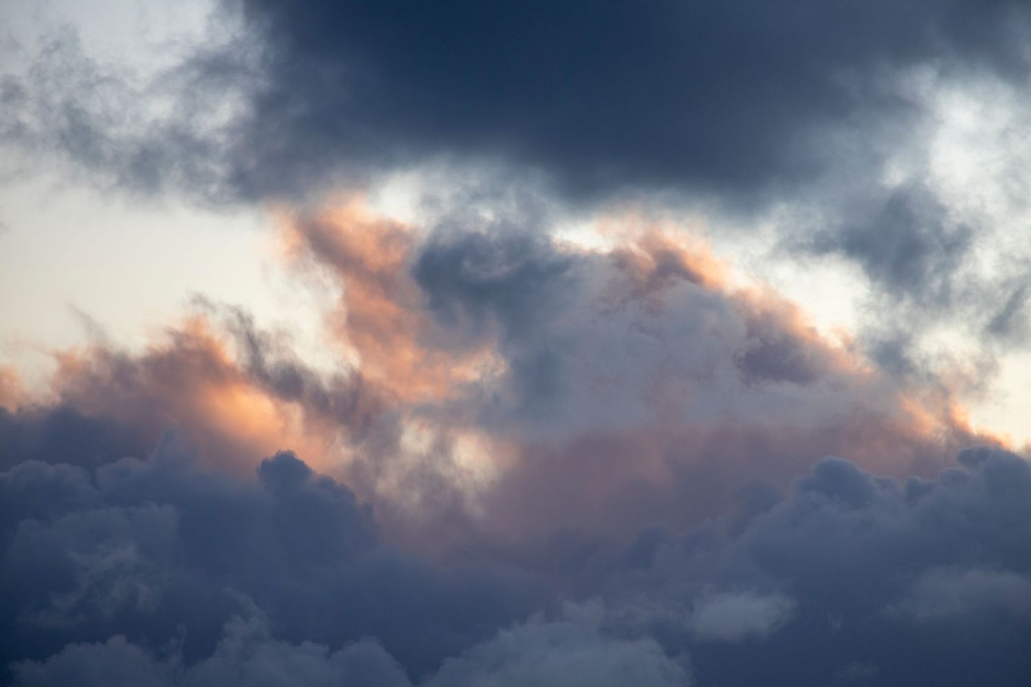 Pink and gold hues break through dark storm clouds, casting an ethereal glow across the sky.