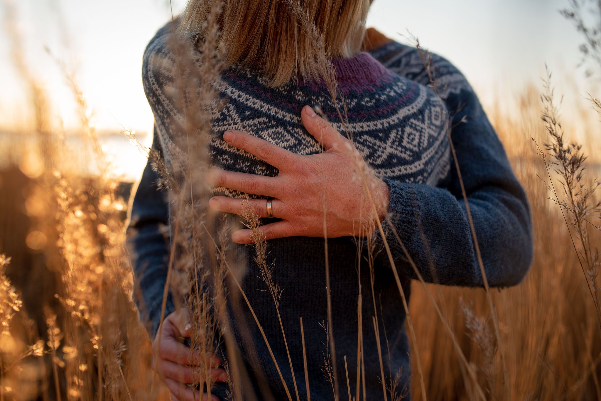 Close-up of hands holding a knit sweater against golden sunset light through tall grass.