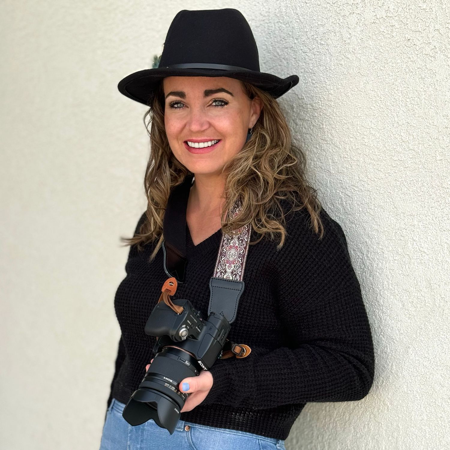 A portrait photo of Kristin holding a camera and wearing a black hat for the website WhiteFlamingoPhotos.com