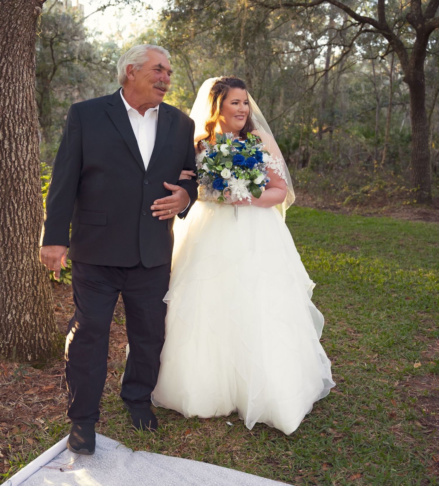 A couple walking through a scenic wooded area during their wedding photo session.