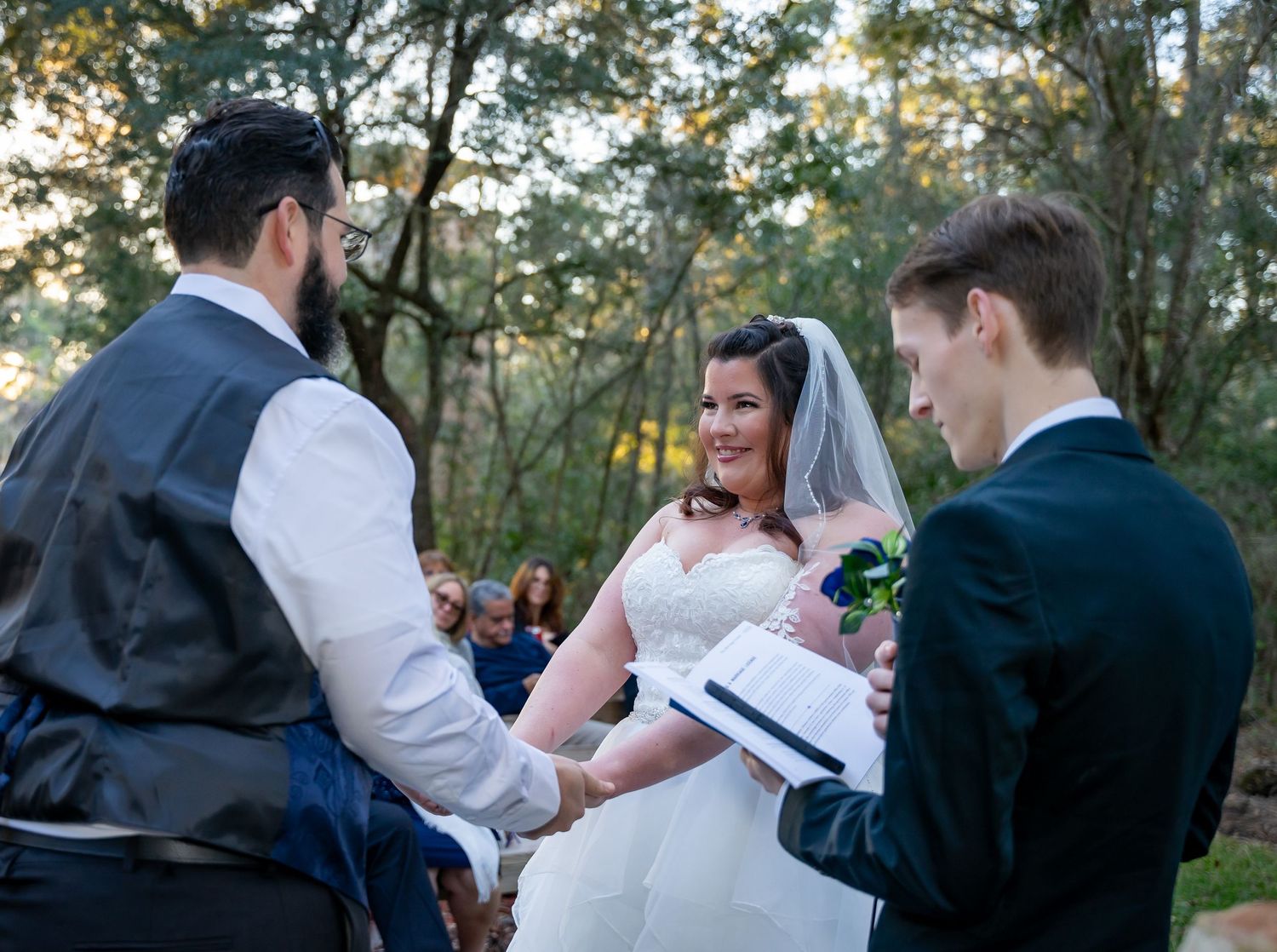 Wedding party gathers under oak trees during an outdoor ceremony.