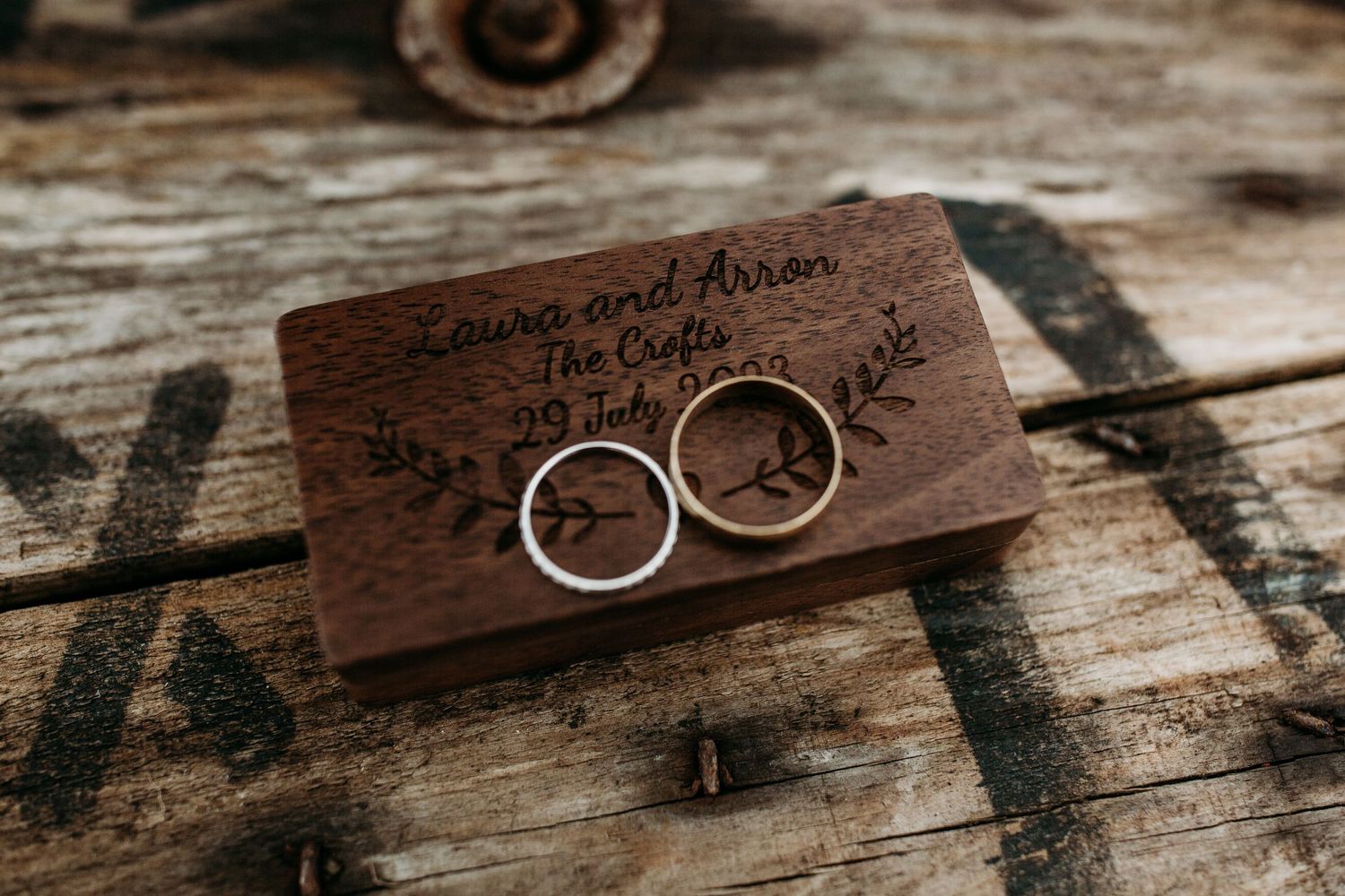 Two wedding rings displayed on a rustic wooden block with engraved text.