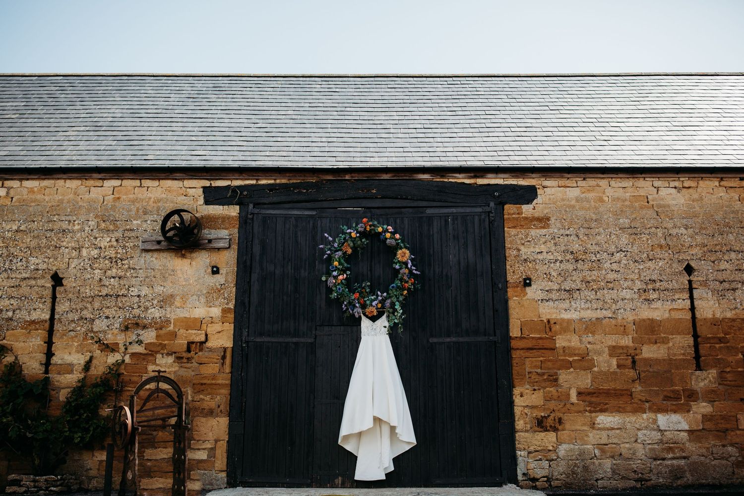 White wedding dress hanging on black barn door with festive wreath.