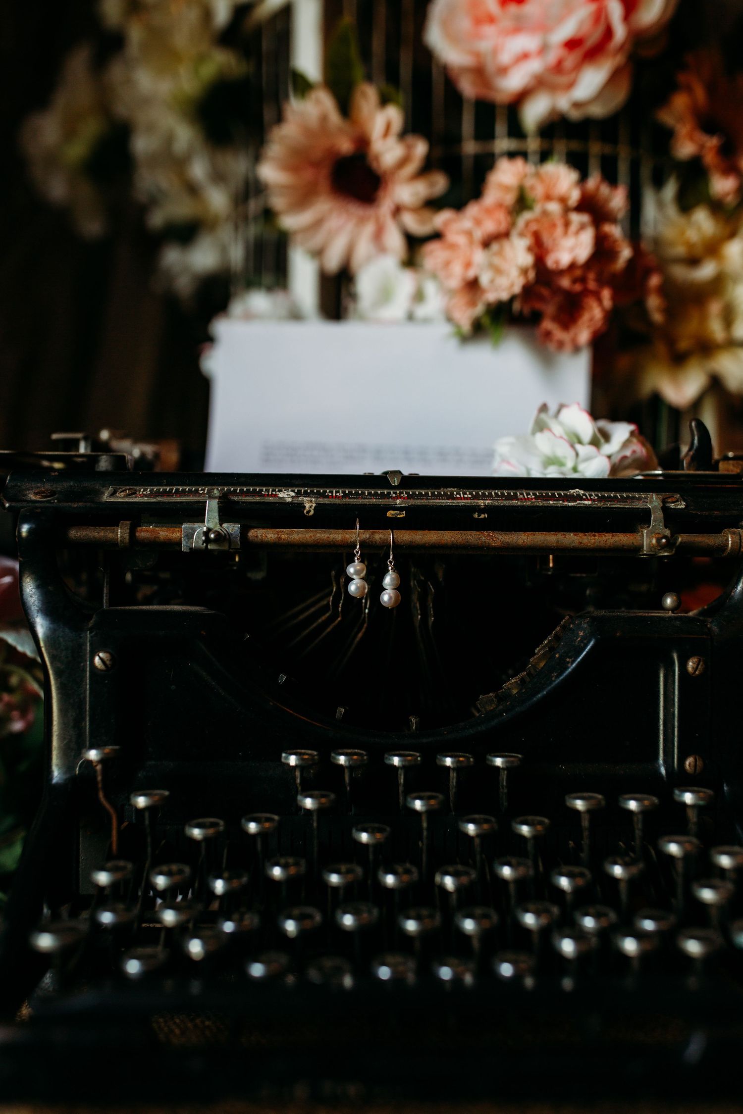 Vintage typewriter with pink and peach flowers displayed above on dark moody background.