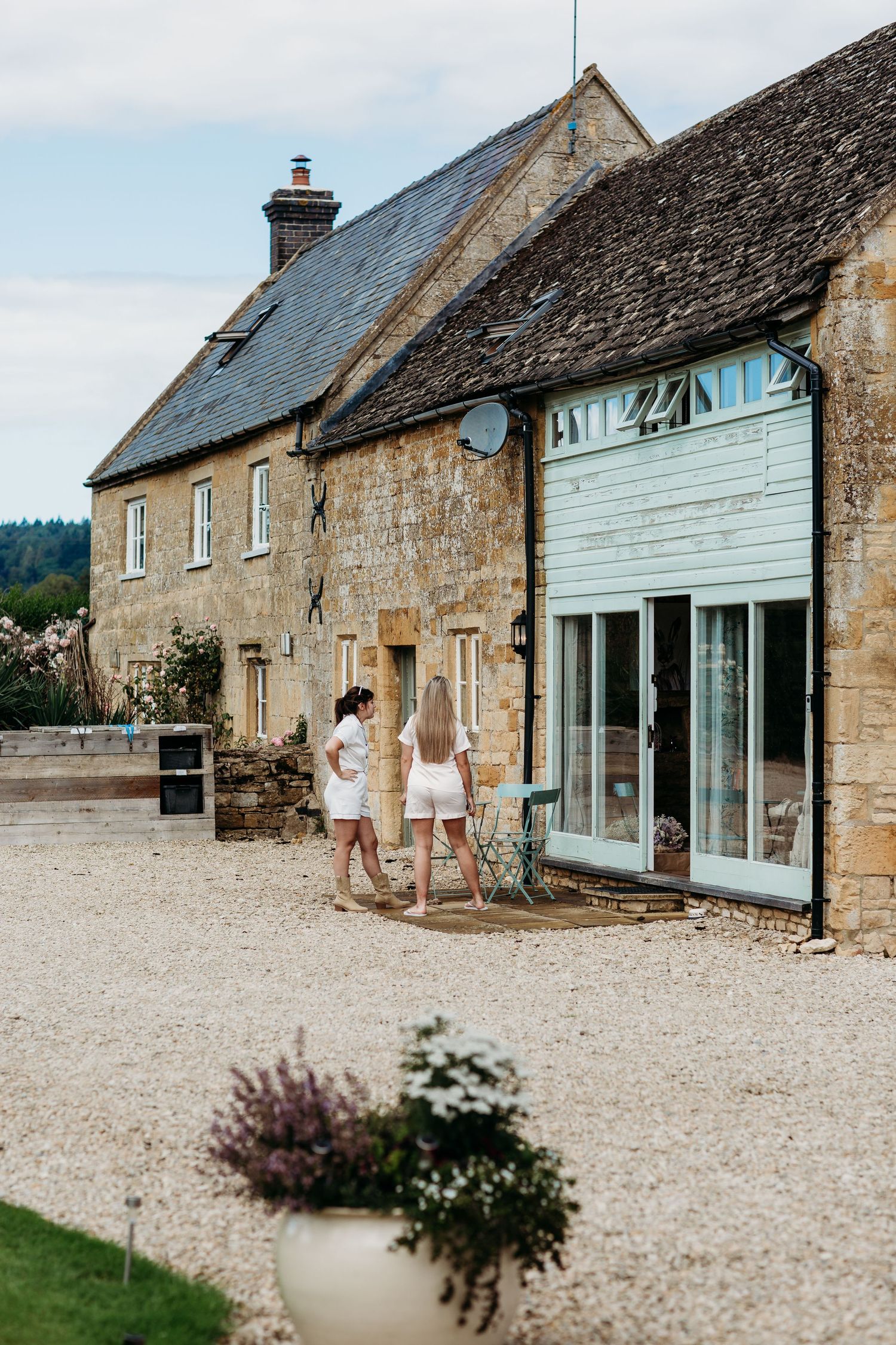 A quaint stone cottage with white shutters and a gravel driveway.