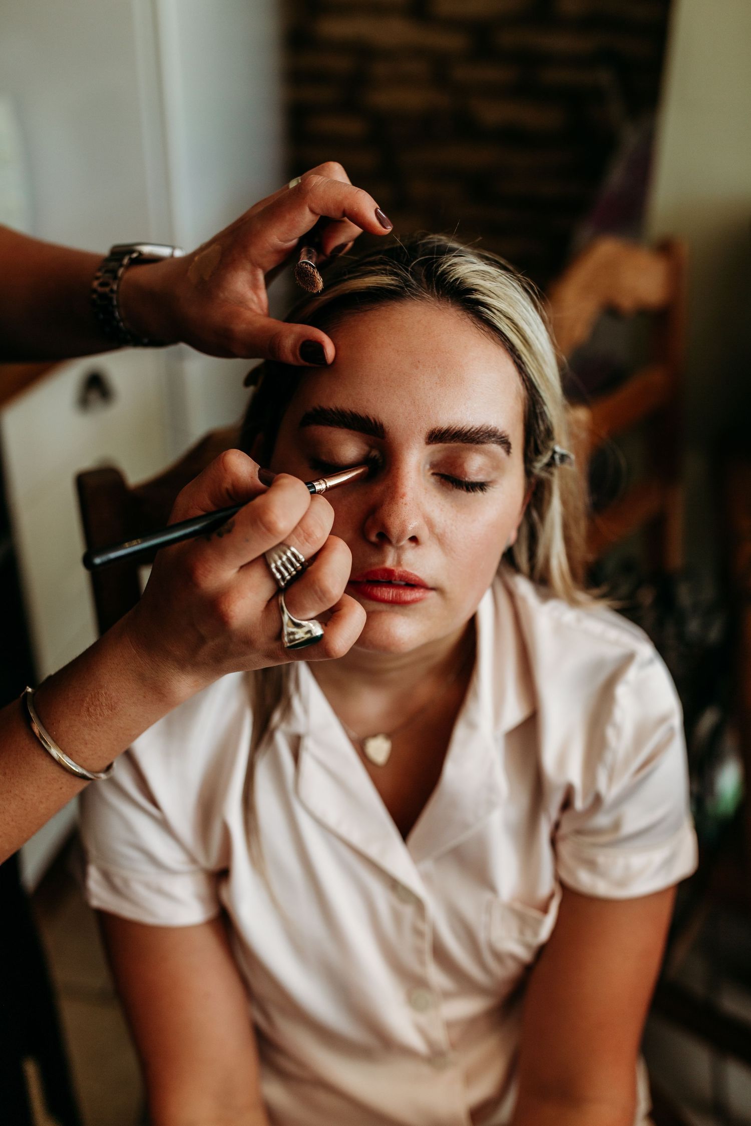 An intimate moment during bridal makeup application with soft natural lighting.