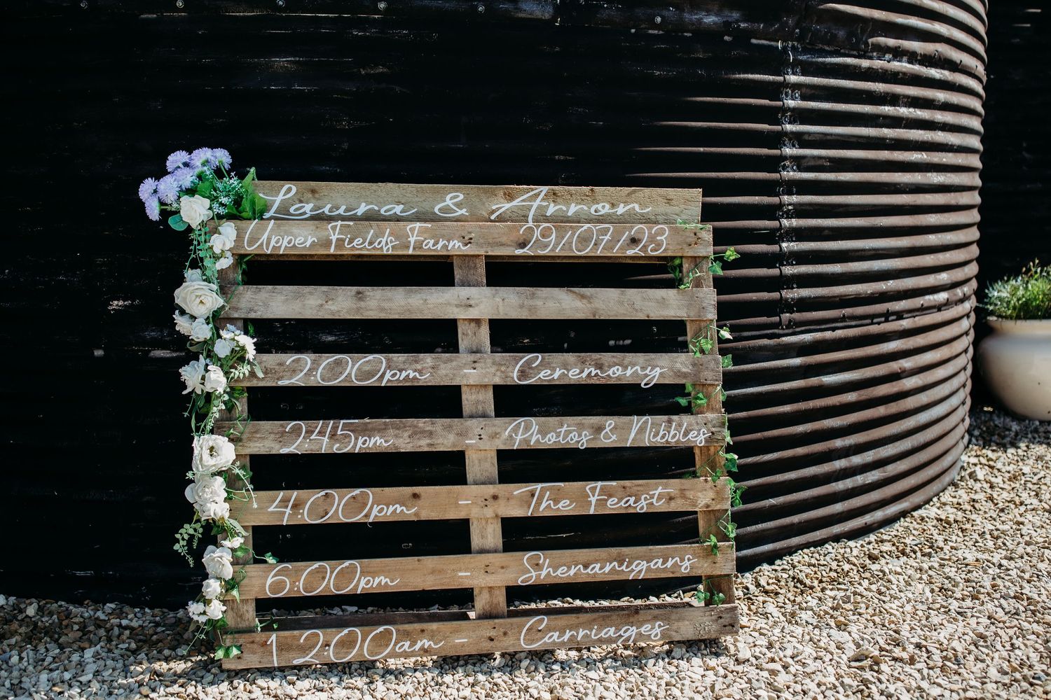 Decorative wooden pallet seating chart adorned with floral accents.