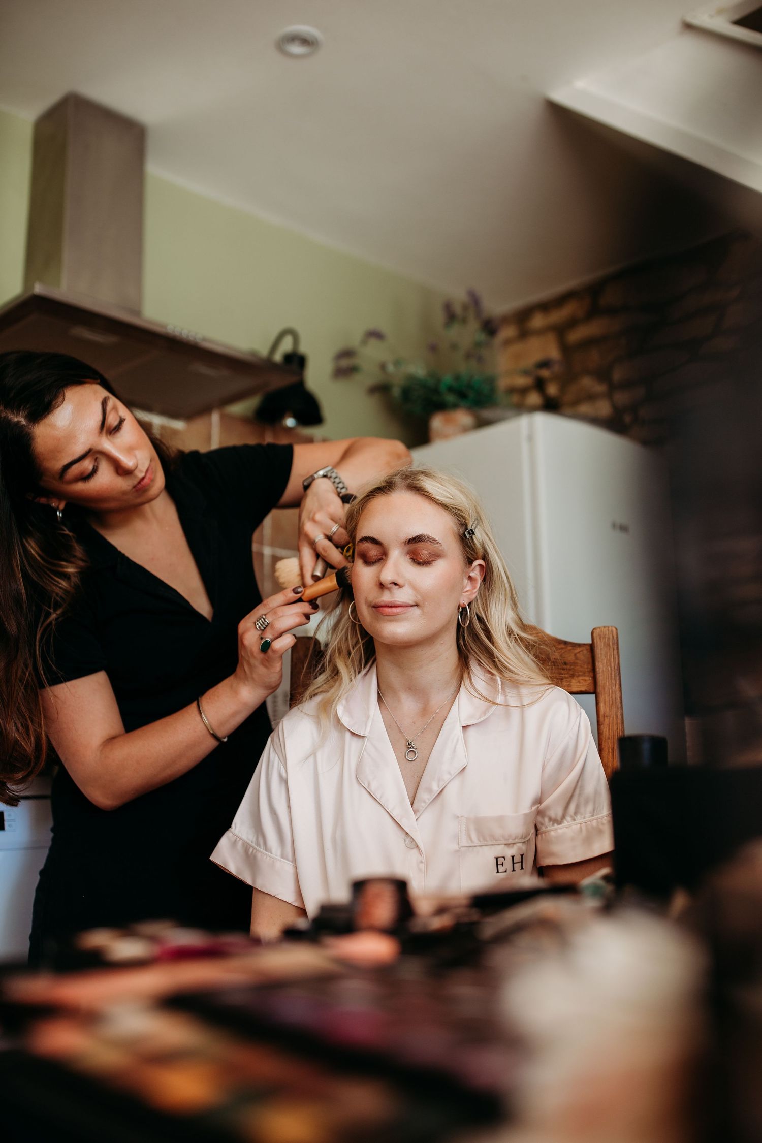 Makeup artist applying cosmetics in cozy kitchen setting.