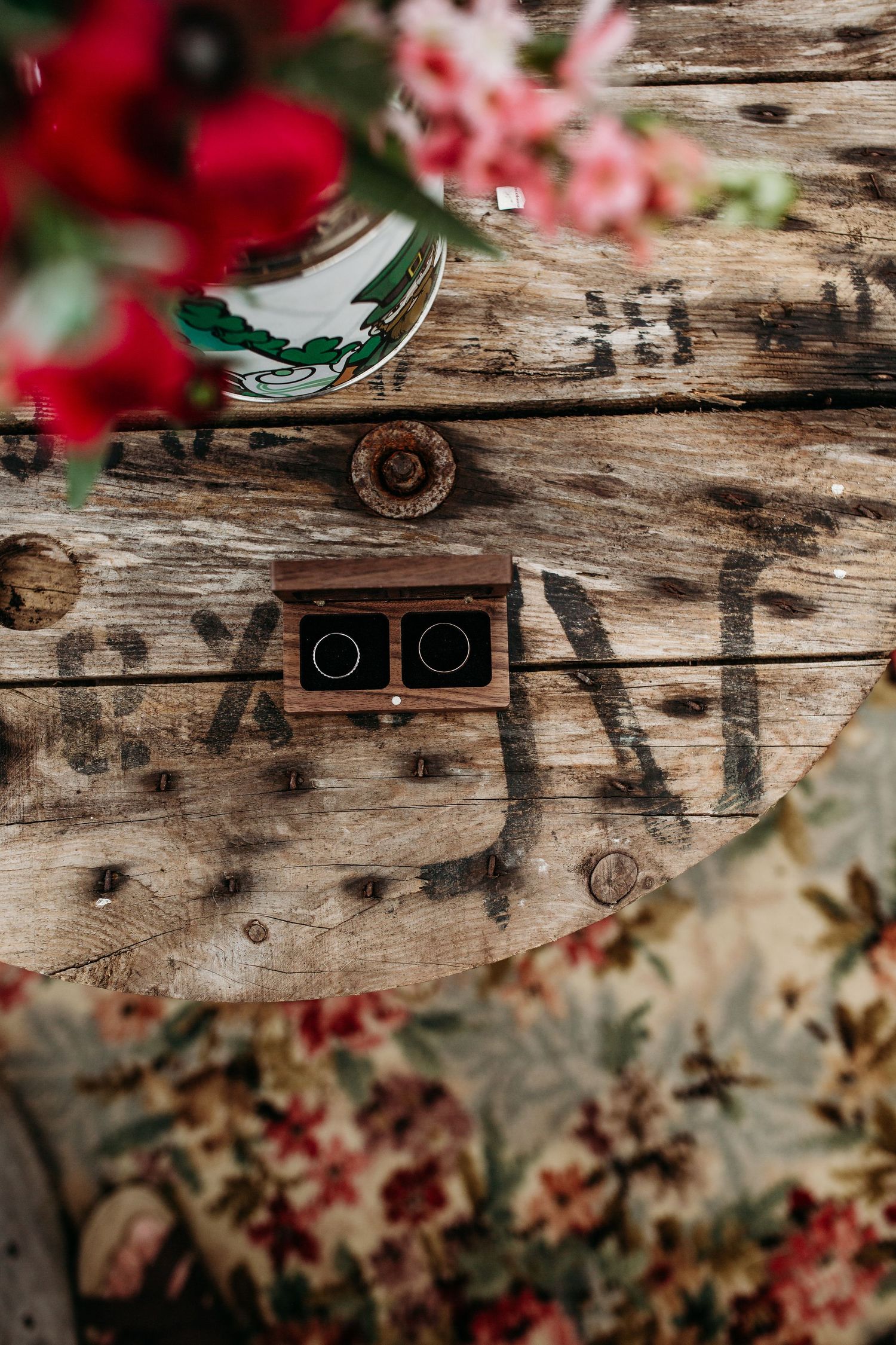 Wedding rings in decorative box with red flowers on weathered wood surface.