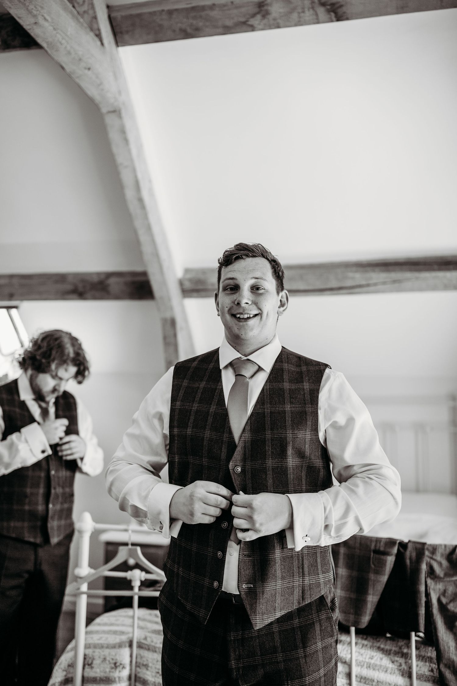 Person wearing plaid vest and tie smiling during wedding preparation.