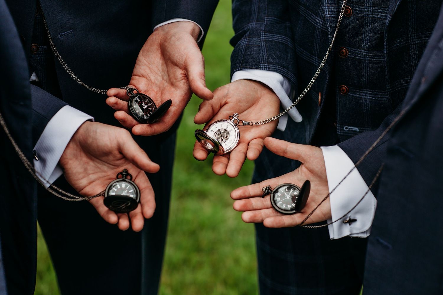 Hands holding pocket watches showing details of wedding party accessories.