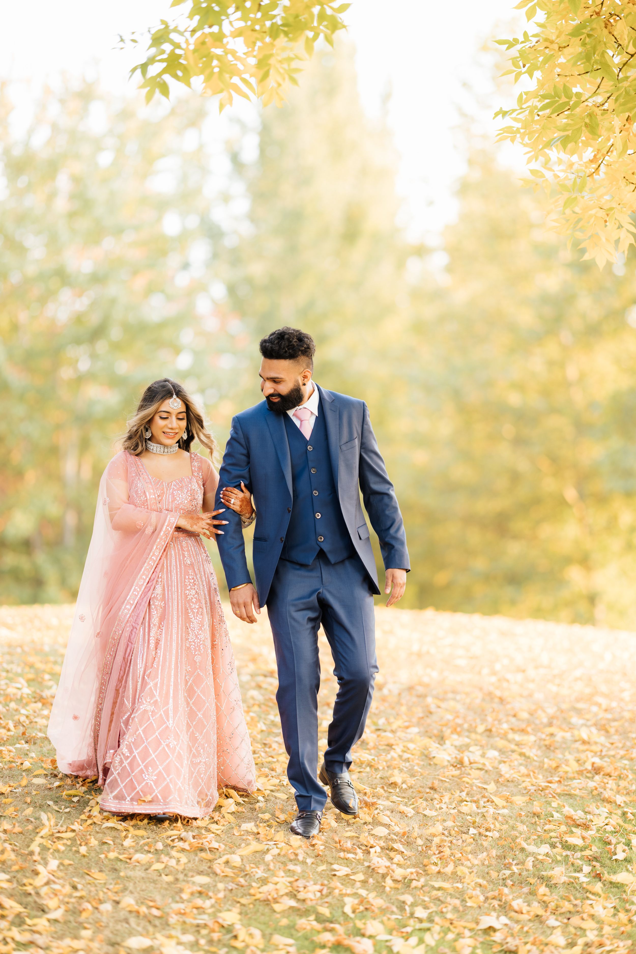 Couple walking hand in hand through fallen autumn leaves in formal attire.