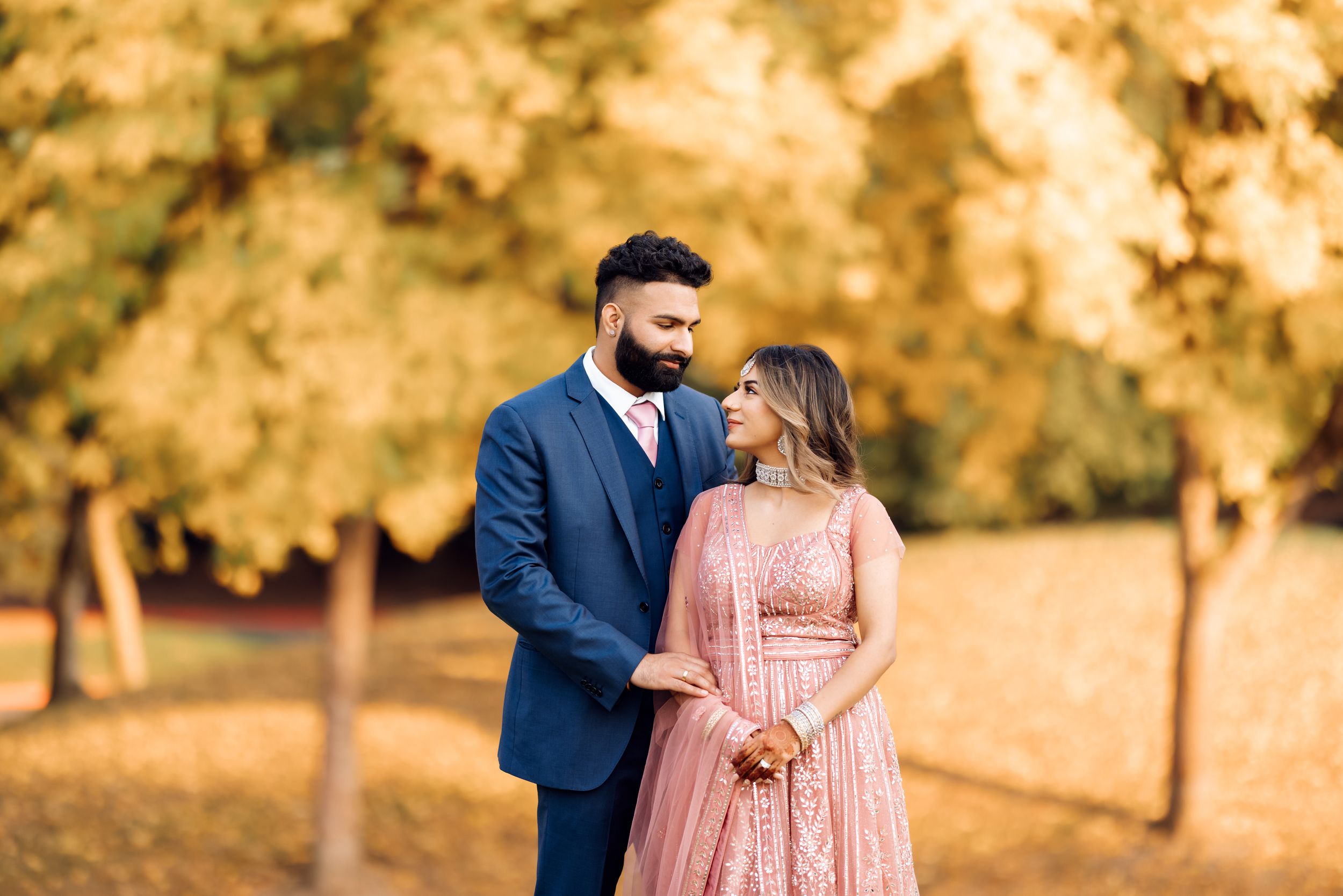 Romantic couple in formal wear standing together in a park with golden autumn trees.