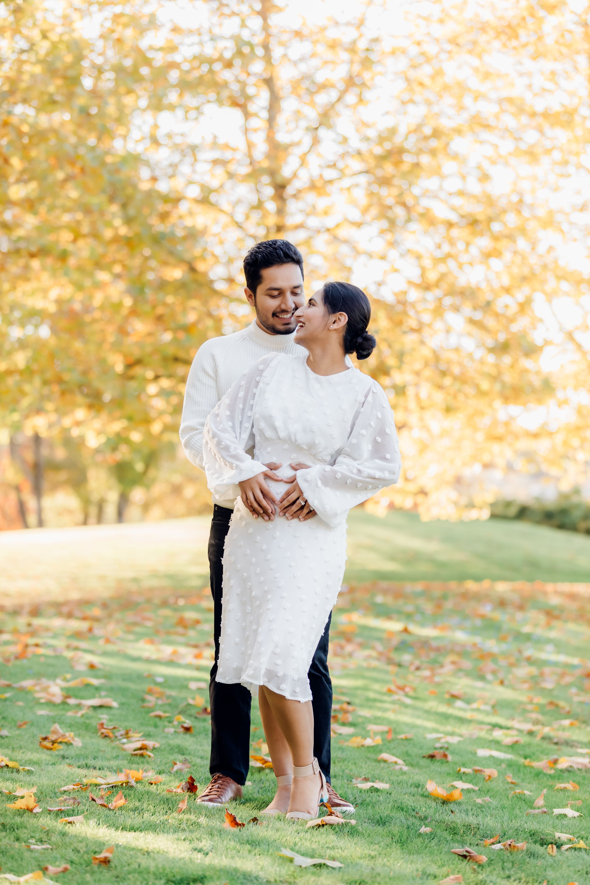 A couple in white outfits shares an intimate moment among autumn trees.