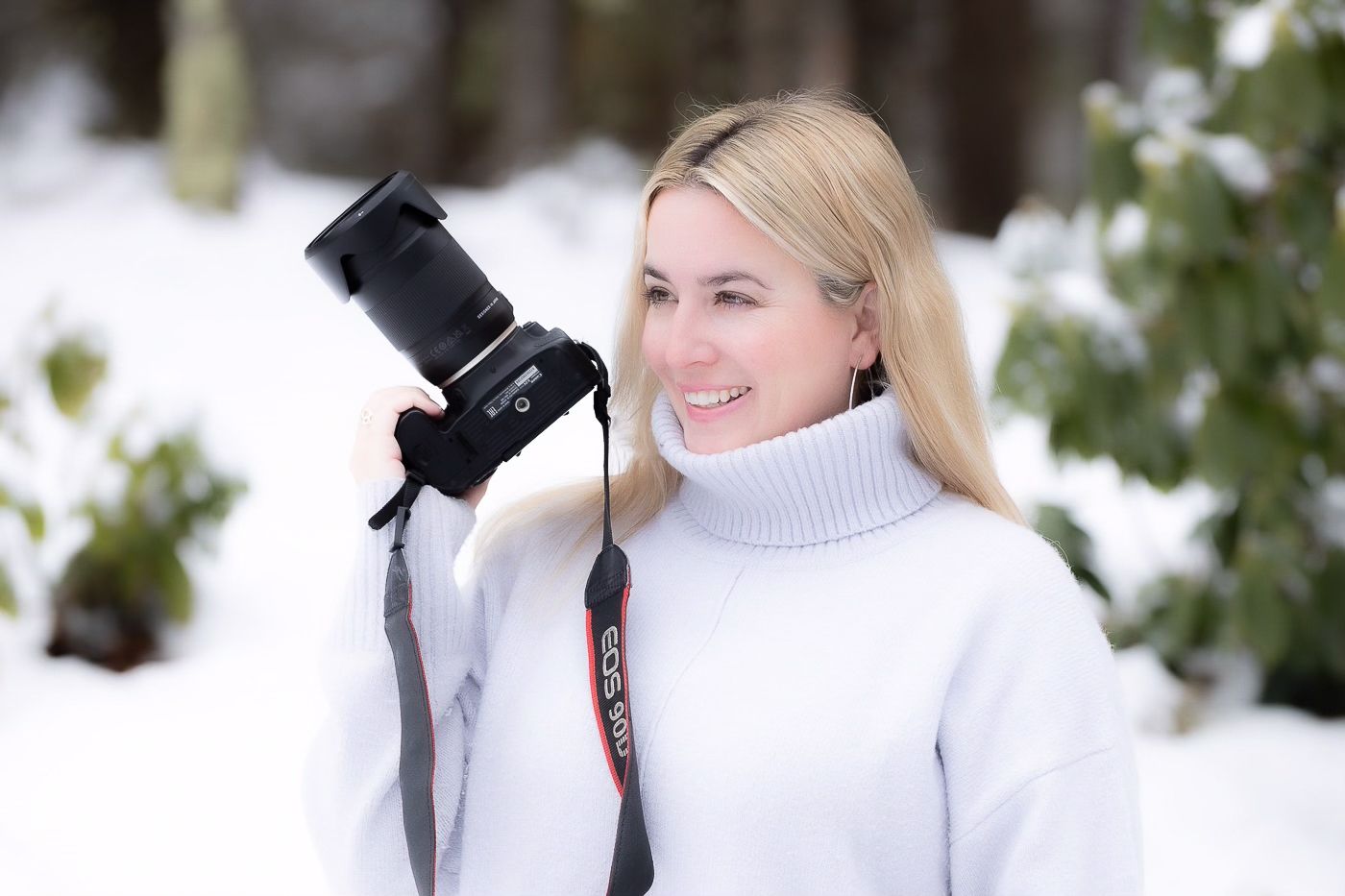 Photographer wearing white sweater holds camera in snowy winter setting.