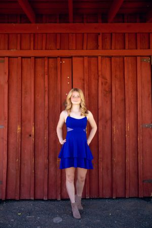 Woman in bright blue dress poses against rustic red barn door.