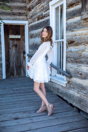 White lace dress twirls on rustic cabin porch with weathered wood walls.