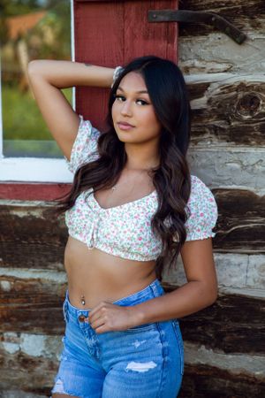 Someone in a floral crop top and jeans poses against a rustic wooden wall.