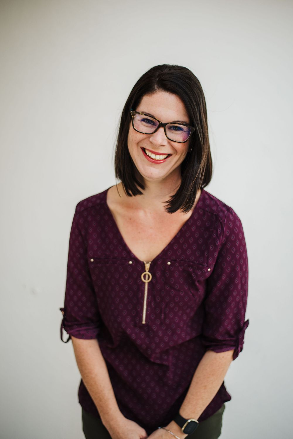 Professional headshot of someone wearing glasses and a burgundy polka dot top against a light background.