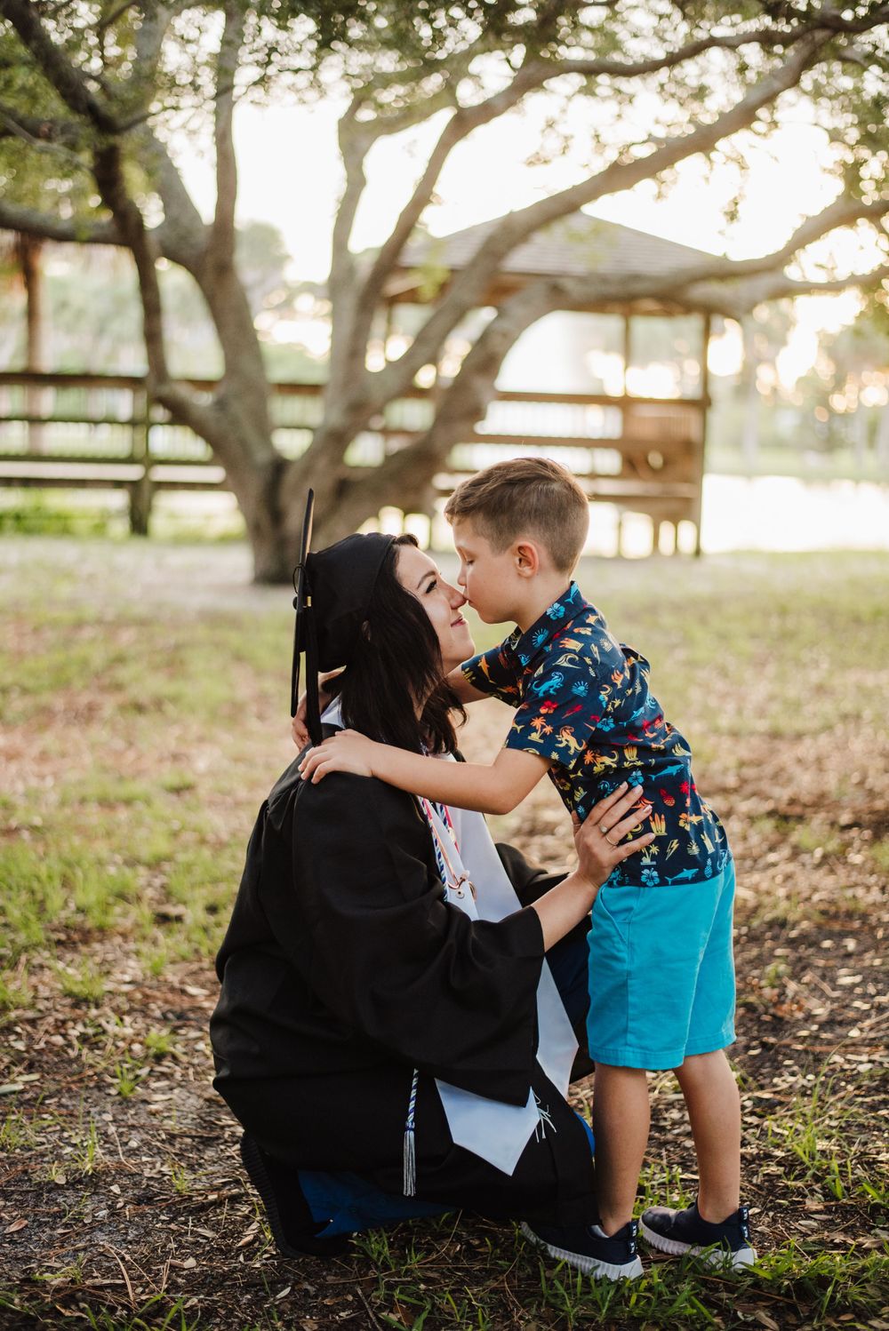 Sweet graduation moment between parent and child under a tree at sunset.