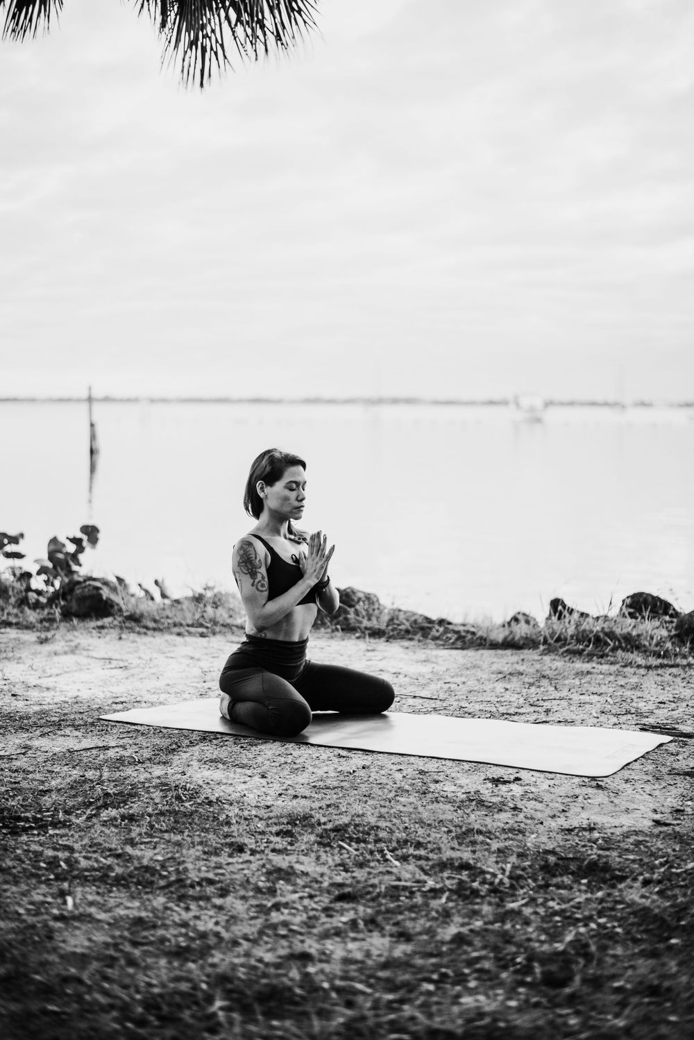 Person meditating on yoga mat outdoors in black and white photography.