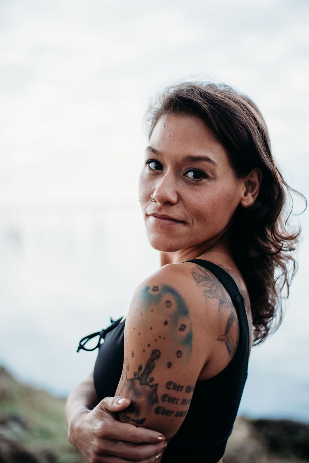 Athletic person in black tank top with artistic tattoo against bright background.