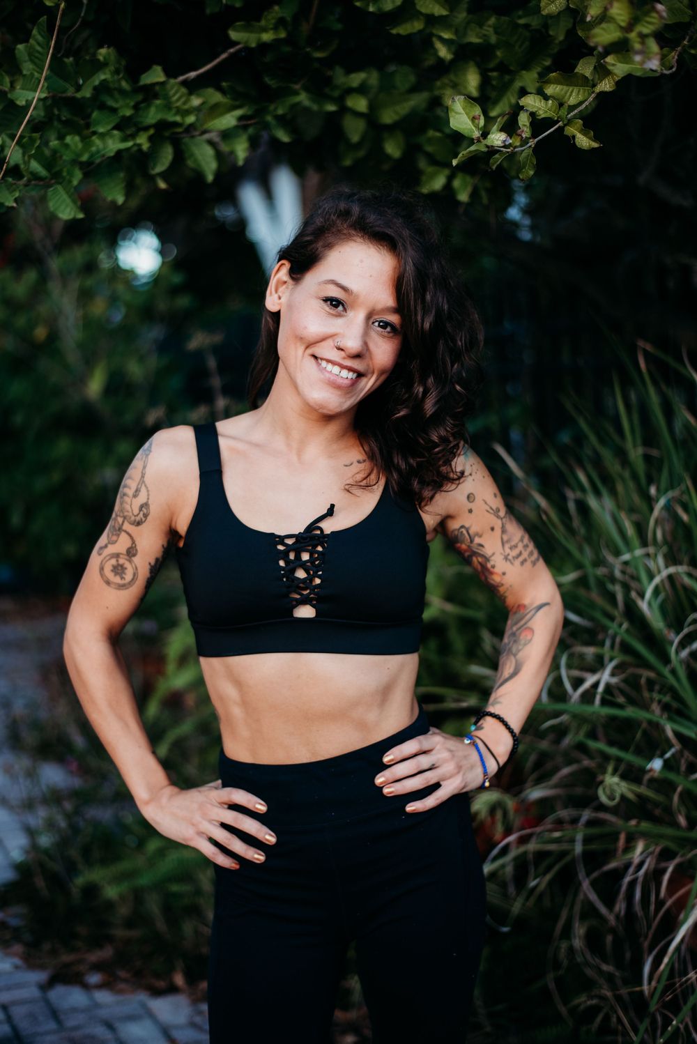 Fitness enthusiast in black workout attire posing outdoors with visible tattoos.