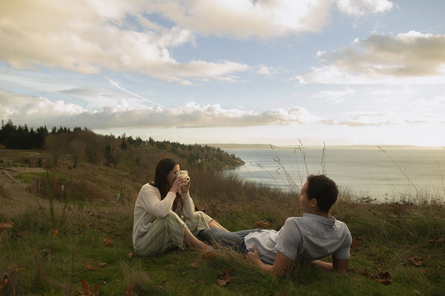 Couple lounging on grass overlooking scenic coastal view at sunset.