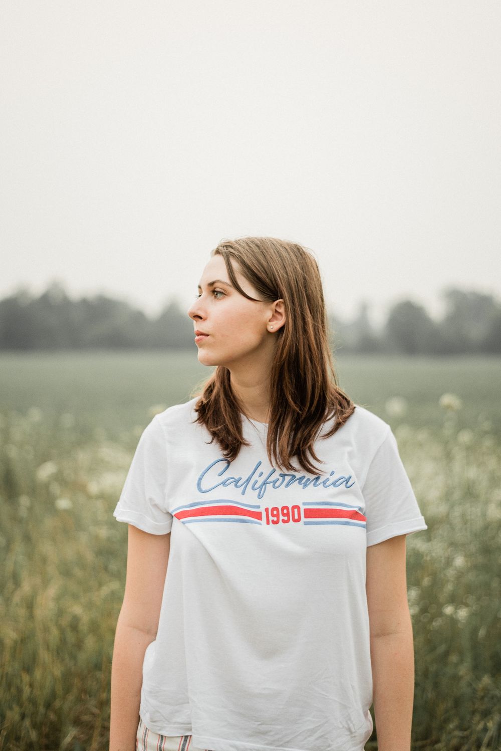 Someone in a white California 1990 t-shirt poses in a dreamy meadow setting.