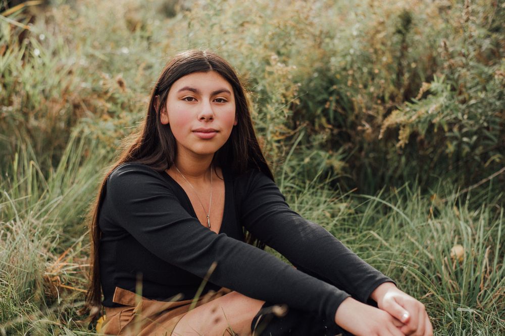 Someone in black sweater sits in tall grass during golden hour portrait session.