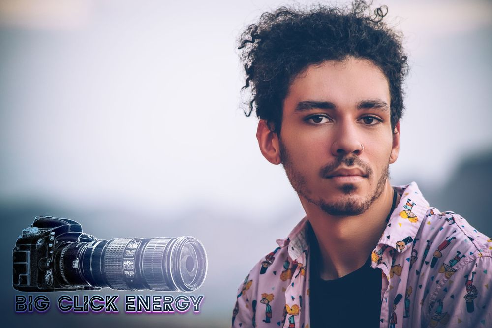 Young man with natural hair and a nose ring, posing outdoors in the desert with a cool blue tone.
