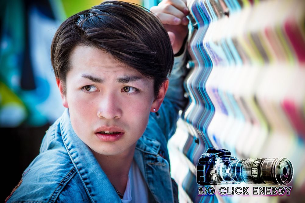Cute Japanese male model posing outdoors in Phoenix, AZ, with a cactus and colorful mural backdrop.