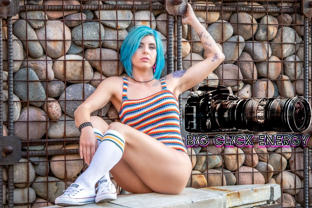 Beautiful female model with blue hair, wearing a colorful crochet swimsuit, posing outdoors in a sexy yet cute style.
