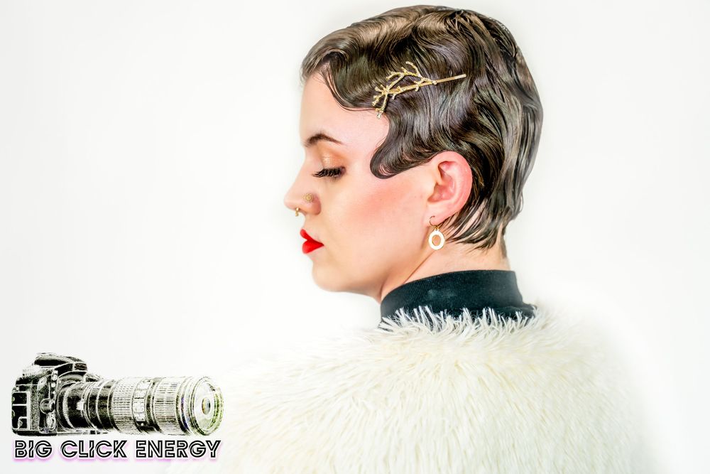 Model with dark brown hair, black gauzy clothes, and a white faux fur coat. 1920s style hair and makeup, soft & edgy.