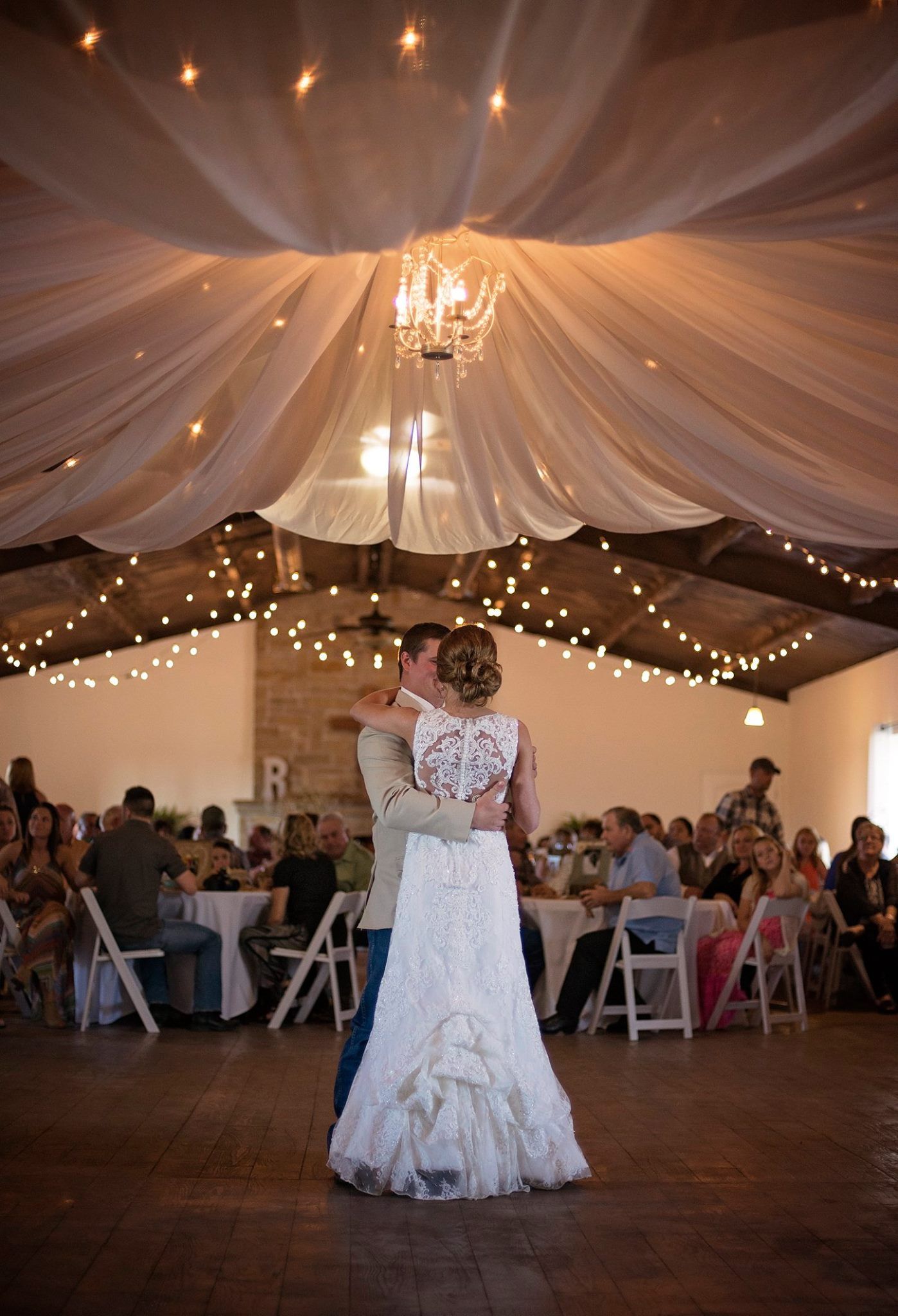 Wedding reception venue decorated with draped fabric ceiling, twinkling lights and elegant chandeliers.