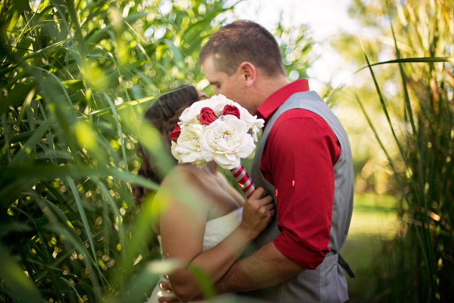 Wedding couple shares romantic moment in lush outdoor garden setting with natural sunlight filtering through trees.