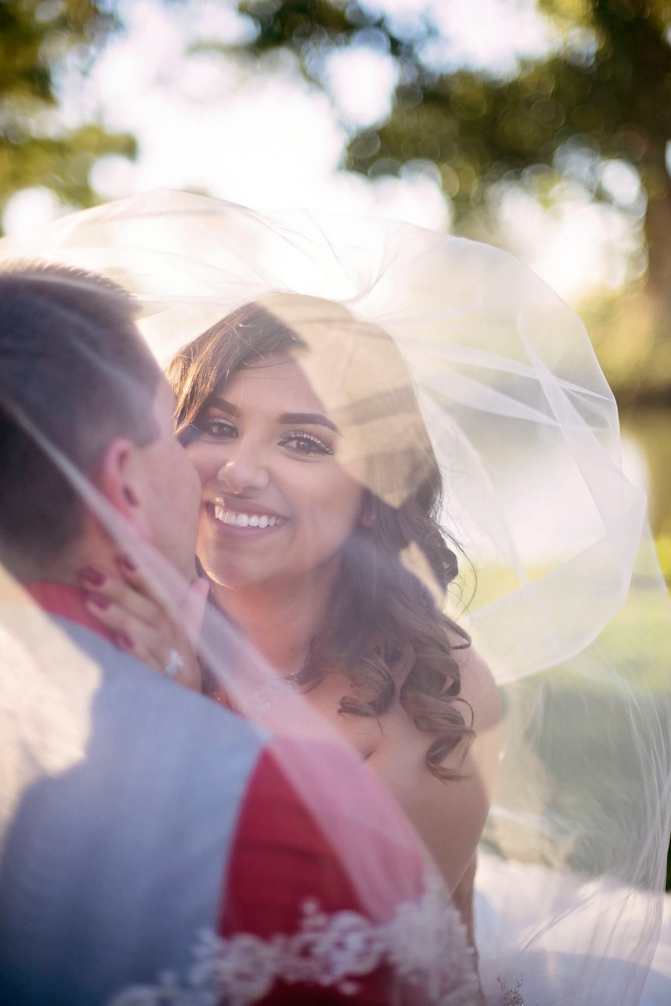 Romantic wedding portrait with soft sunlight and veil creating dreamy atmosphere.