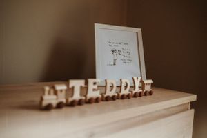 Wooden toy train spelling out text sits on neutral surface in warm lighting.