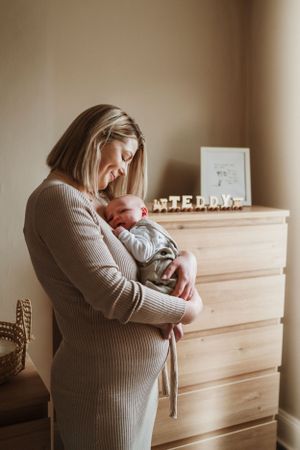 Parent holding newborn near wooden dresser with decorative text display.