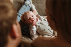 A newborn baby swaddled in white fabric rests peacefully on a soft surface.