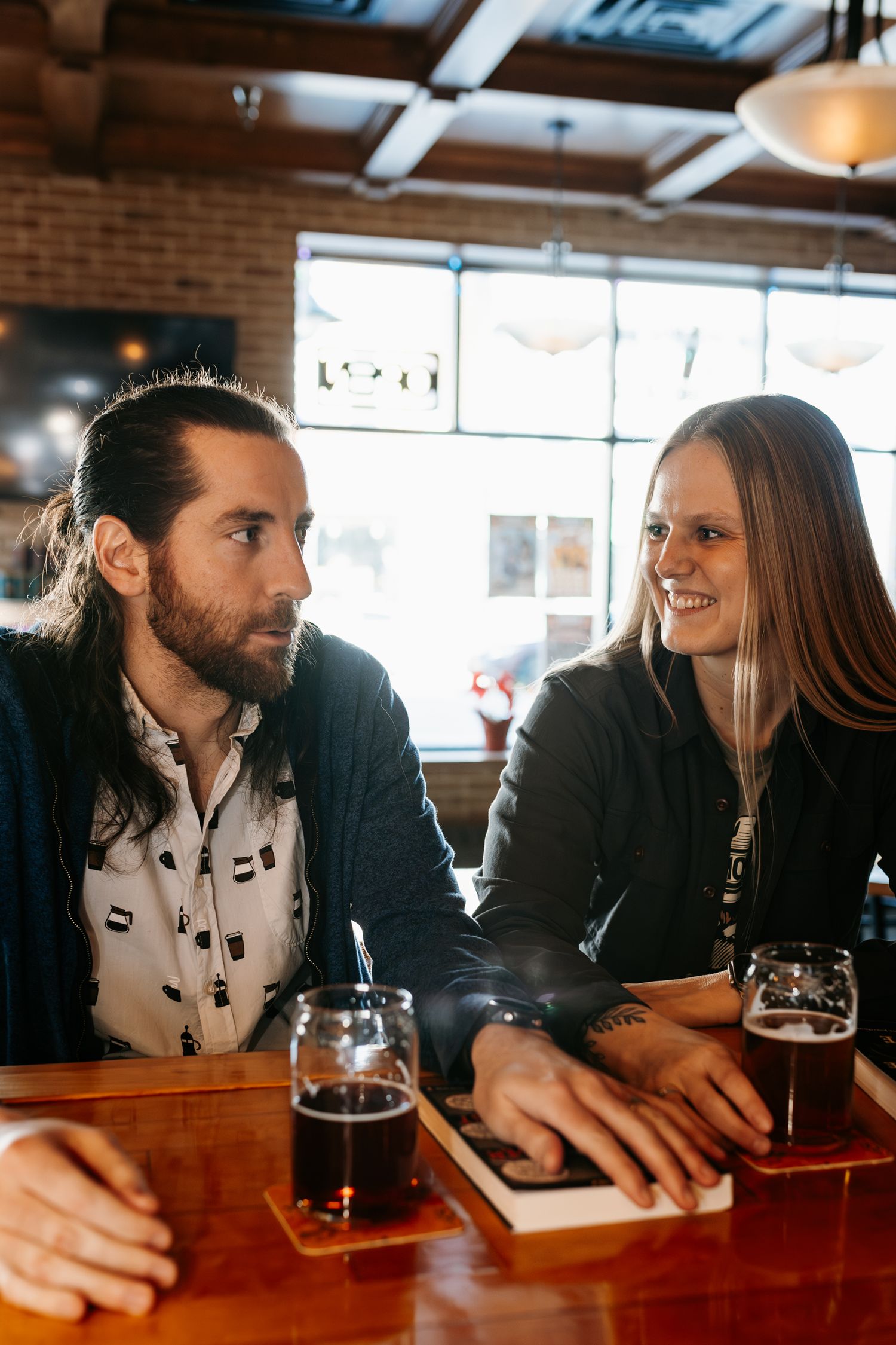 A couple shares drinks and conversation at a cozy bar with exposed brick walls and warm lighting.