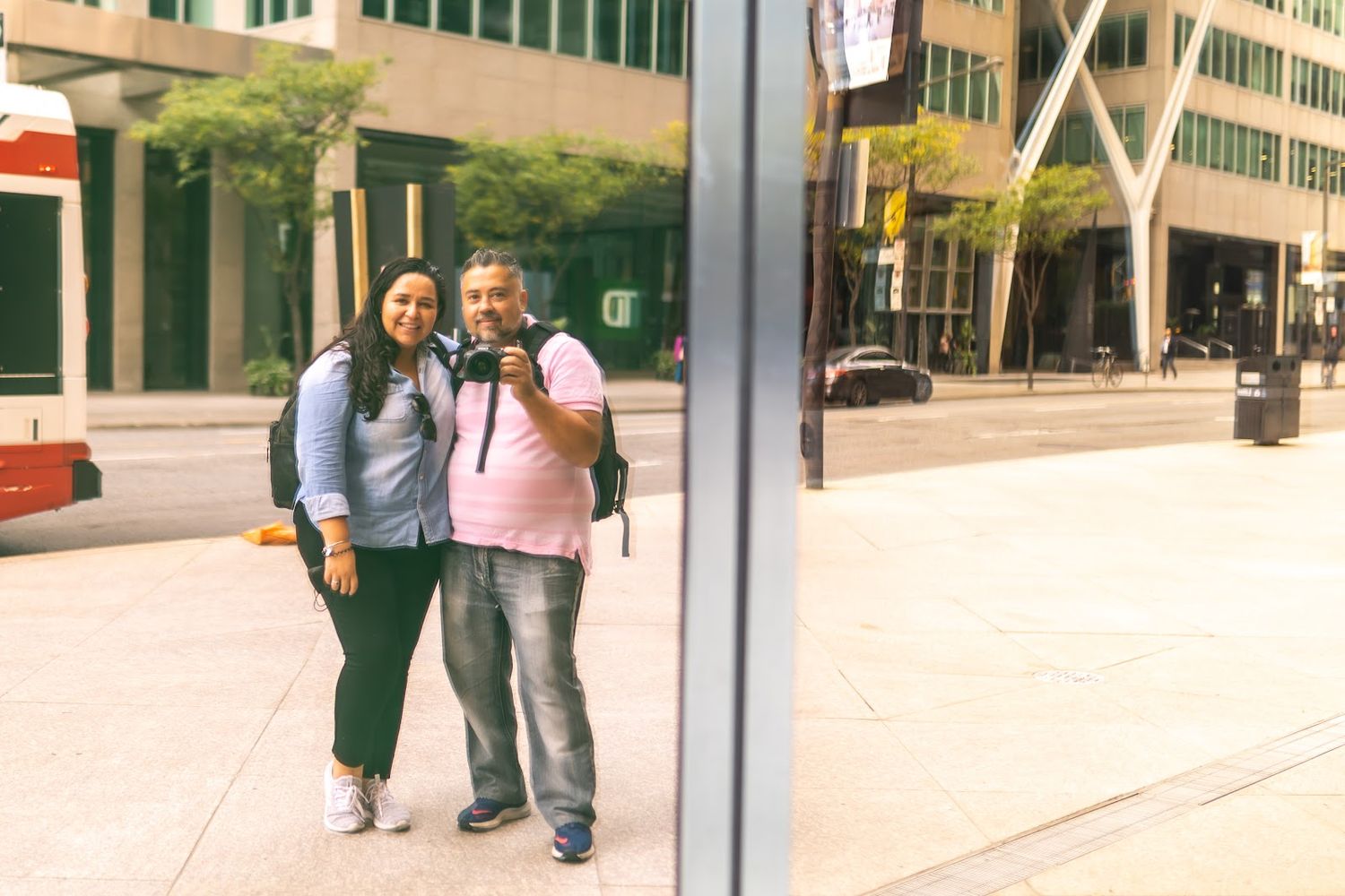 Two people smile together while standing on an urban sidewalk near modern office buildings.