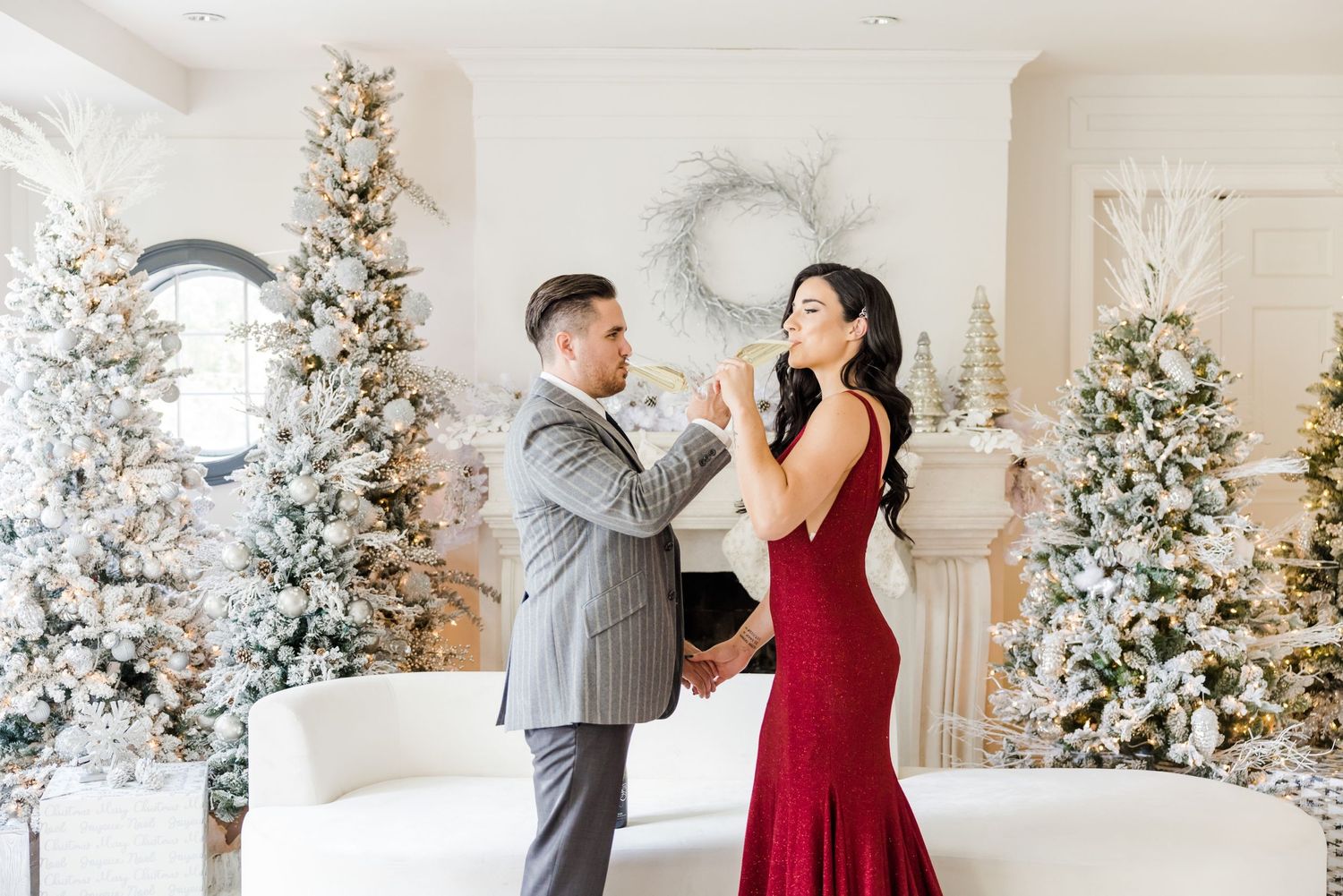 Romantic dance pose between couple dressed in formal attire by Christmas trees.