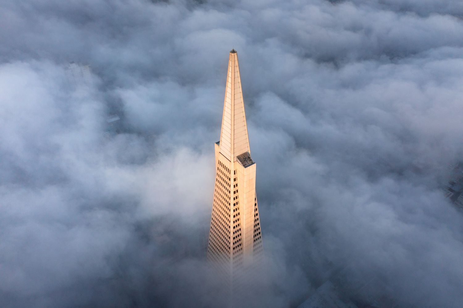 The Transamerica Pyramid skyscraper rises above a blanket of fog in San Francisco during dramatic cloudy conditions.