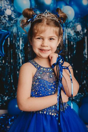 Princess-themed portrait with sparkly blue dress, tiara and festive background.