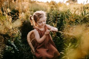 Child in brown dress exploring wildflowers during golden hour sunset.